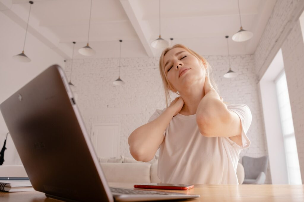 Young beautiful blonde girls sitting behind the laptop. Tired student with pain in the neck. Massage